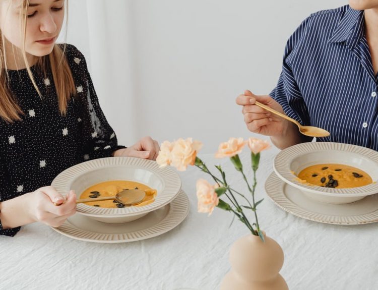 Two women enjoying homemade pumpkin soup at a dining table with floral decor.